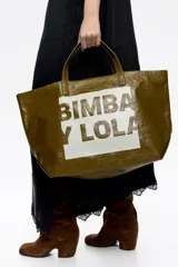 Bolso tipo tote de Bimba y Lola, color dorado con acabado metalizado y efecto arrugado. Presenta un diseño cuadrado con estampado central de la marca en un recuadro oscuro y doble asa de mano en color crema.