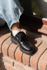 Zapato Oxford negro de cuero con cordones, suela track y detalle de aplique con logo en la lengüeta.