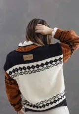Campera tipo bomber tejida en lana merino, con diseño artesanal que combina guardas estilo patagónicas y detalles de flores bordadas. Presenta cierre frontal y terminaciones en tejido acanalado.
