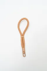 Correa de mano tipo lanyard en color camel, confeccionada en cuerda trenzada con detalles de terminación y mosquetón metálico a tono.