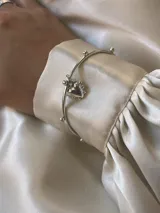 Brazalete esclava de plata con apliques esféricos a lo largo del aro y dije colgante en forma de corazón.