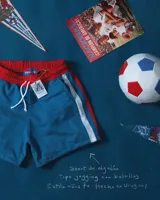 Short de jogging celeste con cintura elástica y cordón blanco. Tiene una franja vertical blanca y roja en los laterales.