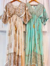 Túnica larga de estilo boho con escote en V profundo, mangas amplias tipo kimono y detalle de cordones con borlas en el frente. Presenta un estampado de arabescos y detalles en hilo metalizado.