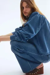 Campera de sarga de mezclilla azul, con cuello elevado, cierre frontal de botones y canesú fruncido. Tiene mangas largas abullonadas con puños ajustados y bolsillos laterales insertados.