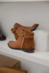 Botas cortas de cuero negro con paneles traseros de gamuza, cierre lateral y detalle de correa con hebilla metálica en el tobillo.