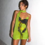 Vestido corto de tirantes finos con escote drapeado, confeccionado en tela semitransparente con estampado abstracto en tonos verdes y negros. Incluye un accesorio tipo pañuelo integrado al cuello.