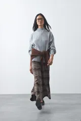 Polera de tejido de punto color gris, con cuello alto, mangas largas abullonadas con puños elásticos y costura central vertical en el frente. Presenta una abertura sutil en la espalda.