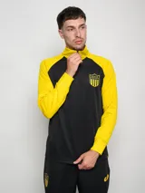 Buzo deportivo de entrenamiento, color negro en el torso y amarillo en las mangas y cuello. Es de manga larga, con cuello alto y cierre parcial frontal. Presenta un escudo con estrellas en el pecho.