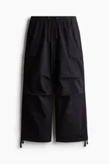 Pantalón cargo negro de corte holgado, con cintura elástica ajustable con cordón, bolsillos laterales al bies, bolsillos tipo cargo con solapa y botón a presión en las piernas y bolsillos traseros con solapa y botón a presión. Cuenta con pliegues cosidos en las rodillas y cordón ajustable oculto en el bajo.