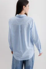 Camisa de corte clásico con cuello camisero, manga larga con puños abotonados y cierre frontal con botones. Presenta un diseño de rayas verticales finas en color negro sobre fondo blanco.