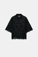 Camisa de encaje negro con cuello solapa, manga corta y cierre frontal con botones.