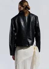 Chaqueta corta de cuero negro con textura efecto cocodrilo, diseño recto, cuello camisero, manga larga, bolsillos laterales de ribete y cierre de doble botonadura.