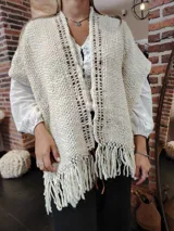 Ruana de lana color crudo tejida a mano, con diseño calado y flecos en el ruedo.