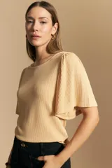 Remera de rib color beige, con cuello redondo y mangas cortas amplias con leve frunce en los hombros. Confeccionada en tejido elastizado de textura acanalada.