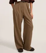 Pantalón de sastrería corte pantalona, color marrón, con cintura alta, pliegues frontales, cierre tradicional y cinturón incluido.