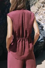 Top fluido sin mangas, de color bordó, con escote en V cruzado y detalle de nudo drapeado en el lateral delantero.