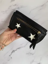 Monedero negro de cuero sintético con diseño de dos estrellas blancas y cierre metálico con tirador.