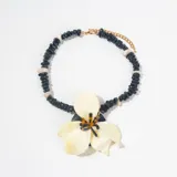 Collar de cuentas negras irregulares con dije central en forma de flor grande de color crema y centro carey.