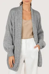 Saco tipo cardigan de punto abierto, color gris, con diseño de mangas largas abullonadas y puños acanalados. Presenta un tejido con sutiles detalles de lentejuelas integradas.