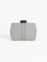 Cartera de mano tipo clutch rígida, con tejido a rayas diagonales en blanco y negro y una franja central con patrón geométrico. Posee un broche de cierre superior rectangular en color negro. Incluye cadena removible.