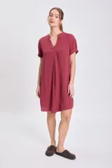 Vestido corto color bordó, de manga corta y escote en V con cuello mao. Presenta un corte holgado con pliegues verticales en la parte delantera.