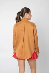 Camisa marrón de lino con cuello mao con volados, manga larga, cierre frontal con botones y bolsillo pequeño en el pecho.