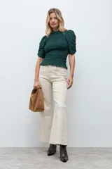 Blusa de color verde oscuro con cuerpo en punto smock, cuello redondo y mangas cortas abullonadas con detalle fruncido. El ruedo presenta un acabado con volado pequeño.