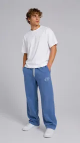 Pantalón de jogging color azul, de corte holgado y diseño recto. Presenta cintura elástica con cordón ajustable y un pequeño logo bordado en color blanco en la parte superior del muslo izquierdo.
