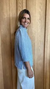 Camisa de manga tres cuartos color beige con cuello con volados y botones frontales. Presenta un detalle de color negro en la parte superior de las mangas.