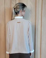 Camisa de manga larga con estampado de rayas verticales en tonos crudo y beige. Presenta cuello alto con volados, cierre frontal con botones dobles y puños con volados.