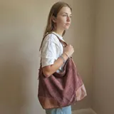 Bolso tipo hobo de eco cuero con textura símil gamuza color marrón rojizo. Presenta detalles de cuero liso color caramelo en la base y tiras ajustables en los laterales.