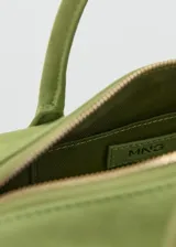 Bolso de mano cilíndrico de cuero gamuzado color verde, con dos asas cortas y detalle de lazo decorativo en un lateral. Cuenta con cierre superior de cremallera.