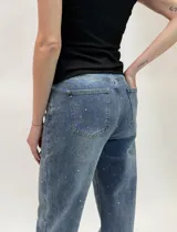 Jean de denim azul con diseño cruzado en la cintura, cierre de botón metálico y aplicaciones de strass en toda la prenda.