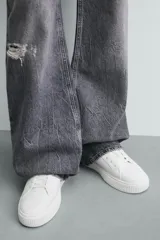 Zapatilla deportiva blanca con suela de plataforma gruesa y texturizada. Presenta detalles en gamuza gris en el lateral y un parche negro en el talón.