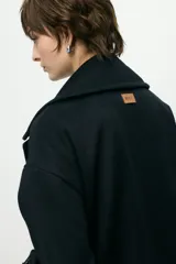 Abrigo de paño de lana con cuello alto estructurado, cierre frontal y mangas largas con detalle de botón en el puño.