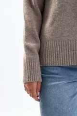 Buzo de tejido de punto en color beige, con cuello redondo a la base, mangas largas y puños y ruedo acanalados.