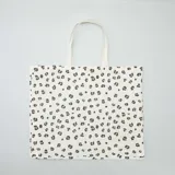Tote bag de tela en color beige con estampado animal print de leopardo en tonos marrones y negros. Cuenta con dos asas largas para llevar al hombro.