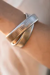 Pulsera rígida plateada de diseño entrelazado y acabado texturizado con líneas paralelas.