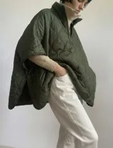 Poncho acolchado color verde oliva, con cuello alto y cierre frontal parcial. Presenta un patrón de costuras acolchadas en forma de círculos.