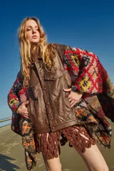 Poncho de cuero ovino con corte de chaqueta y mangas tejidas en lana con diseño geométrico multicolor. Talle único.