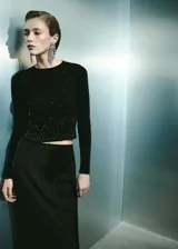 Jersey de punto fino color negro, con cuello redondo y manga larga. Presenta un diseño crop con aplicación de strass distribuido por toda la prenda.