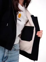 Chaqueta de lona color negro con forro interior de sherpa, cierre frontal con cremallera, capucha y puños elásticos.