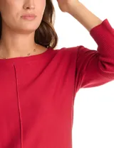 Buzo de tejido fino con cuello redondo, manga tres cuartos con puños acanalados y detalle de pespunte vertical en el frente. Presenta un diseño liso con aplique de botones en la espalda.