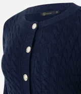 Cárdigan de punto trenzado color marrón, con cuello redondo, manga larga y cierre frontal con botones metálicos. Presenta puños y ruedo acanalados.