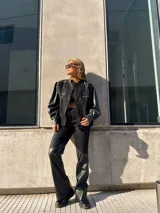 Campera de estilo bomber combinada en denim negro y mangas de cuero sintético, con cierre frontal y bolsillos con cremallera en el pecho.