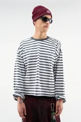 Remera de manga larga oversize con diseño a rayas horizontales en blanco y azul marino, cuello redondo oscuro y estampado en amarillo en la espalda.