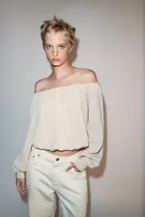 Blusa de punto color beige con cuello barco, manga larga abullonada con puños ajustados y detalles fruncidos en la parte delantera.