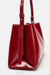 Bolso de hombro en formato mini color rojo, con detalle de pespuntes centrales y asa ajustable. Cuenta con compartimento interior con cremallera y doble compartimento exterior con cierre imantado.