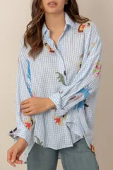 Camisa de corte oversize, con estampa a cuadros vichy en celeste y blanco, complementada con llamativos motivos florales bordados y de manga larga.