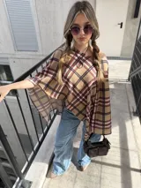 Poncho beige con estampado a cuadros en tonos marrón, negro y rojo, con diseño asimétrico y escote redondo.